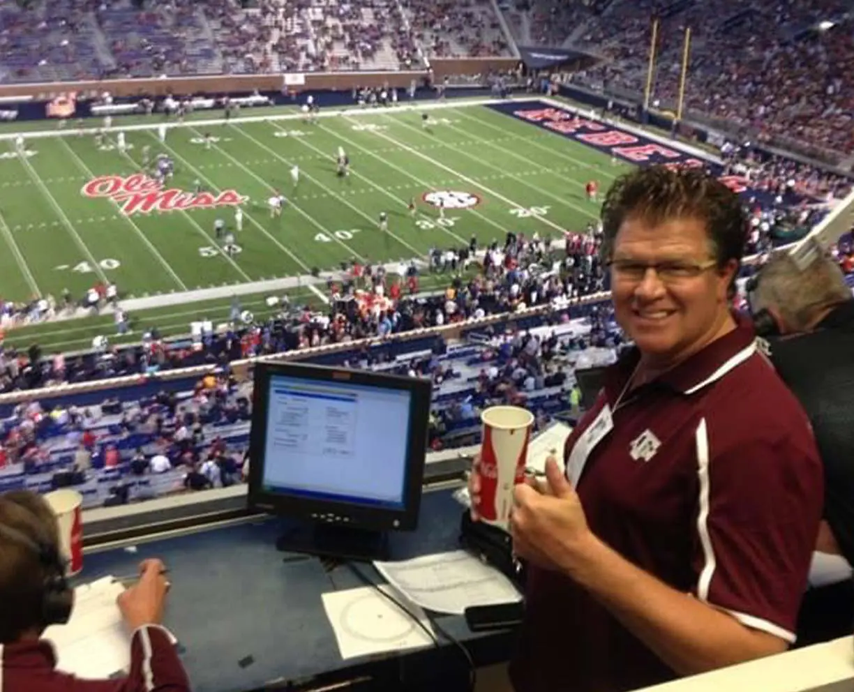 Man in a suite, overlooking football field and giving thumbs up
